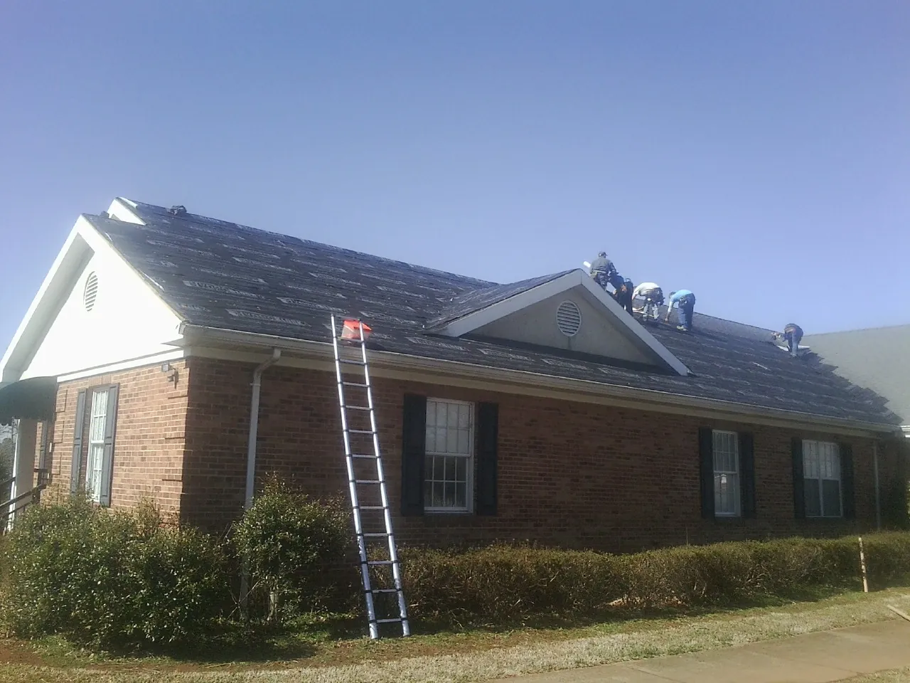 Crew tearing shingles off a brick ranch roof with a ladder set — Emergency Roof Repair work by our crew in Rockford